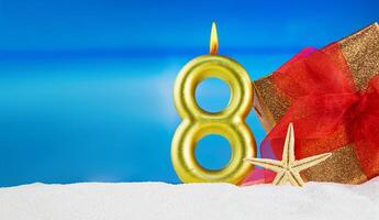 Golden candle number 8 with gift with red bow and starfish on beach. 8th of March, International Women's Day, birthday. Copy space photo