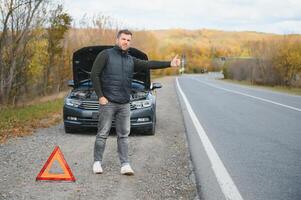 hermoso joven hombre con su coche roto abajo por el borde del camino foto