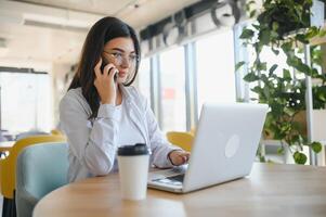 hermosa joven persona de libre dedicación mujer utilizando ordenador portátil computadora sentado a café mesa. contento sonriente niña trabajando en línea o estudiando y aprendizaje mientras utilizando cuaderno. Lanza libre trabajar, negocio personas concepto. foto