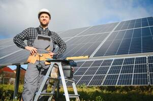 retrato de sonriente confidente ingeniero técnico con eléctrico destornillador, en pie en frente de inconcluso alto exterior solar panel foto voltaico sistema