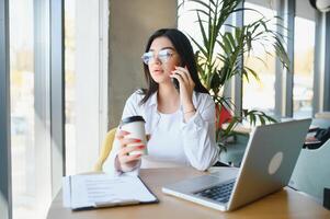 hermosa joven persona de libre dedicación mujer utilizando ordenador portátil computadora sentado a café mesa. contento sonriente niña trabajando en línea o estudiando y aprendizaje mientras utilizando cuaderno. Lanza libre trabajar, negocio personas concepto. foto