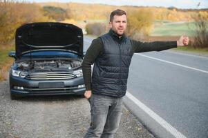 un joven hombre con un negro coche ese rompió abajo en el camino, copia espacio. foto