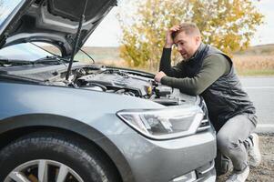 driver trying to figure out how to fix broken down car with red triangle to warn other road users photo