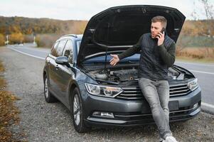 hermoso joven hombre vocación para asistencia con su coche roto abajo por el borde del camino foto