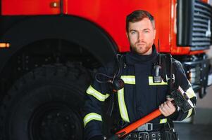 Photo of young fireman with sledgehammer in hands near fire engine