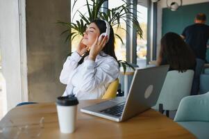 hermosa joven persona de libre dedicación mujer utilizando ordenador portátil computadora sentado a café mesa. contento sonriente niña trabajando en línea o estudiando y aprendizaje mientras utilizando cuaderno. Lanza libre trabajar, negocio personas concepto. foto