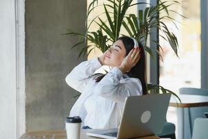 negocio mujer estilo de vida Lanza libre sentado solo él utilizando auriculares escuchando música nuevo canción durante trabajando en ordenador portátil computadora en café café comercio, estudiante niña café descanso mientras haciendo deberes foto