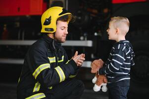 retrato de rescatado pequeño chico con bombero hombre en pie cerca fuego camión. bombero en fuego luchando operación. foto