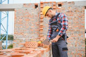 Using bricks. Young construction worker in uniform is busy at the unfinished building photo