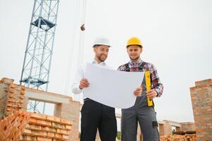 engineer and builder in hard hats discussing blueprint on construction site. photo