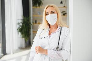 medio años rubia mujer vistiendo médico uniforme y médico máscara en pie a clínica foto