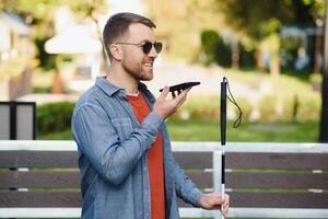 Young blinded man using phone and sending voice message photo