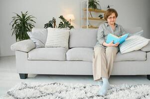 Old lady sitting on couch and enjoying interesting novel stock photo