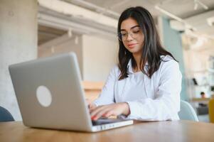 hermosa joven persona de libre dedicación mujer utilizando ordenador portátil computadora sentado a café mesa. contento sonriente niña trabajando en línea o estudiando y aprendizaje mientras utilizando cuaderno. Lanza libre trabajar, negocio personas concepto. foto