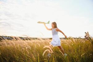 Happy girl runs with a toy airplane on a field in the sunset light. children play toy airplane. teenager dreams of flying and becoming a pilot. girl wants to become a pilot and astronaut. Slow motion. photo