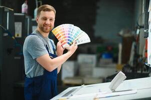 Man worker measuring printing color with spectrometer on the operating desk of the printing plant photo