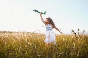 contento niña carreras con un juguete avión en un campo en el puesta de sol ligero. niños jugar juguete avión. adolescente Sueños de volador y convirtiéndose un piloto. niña quiere a volverse un piloto y astronauta. lento movimiento. foto