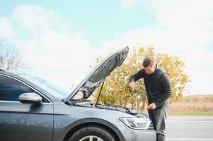 driver trying to figure out how to fix broken down car with red triangle to warn other road users photo