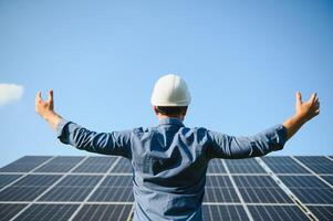 contento trabajando solar estación levantamiento su manos en un antecedentes de fotovoltaica paneles Ciencias solar energía foto