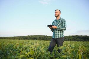 Young agronomist holds tablet touch pad computer in the soy field and examining crops before harvesting. Agribusiness concept. agricultural engineer standing in a soy field with a tablet in summer. photo
