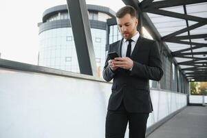 retrato de un emocionado joven empresario vestido en traje participación móvil teléfono, celebrando. foto