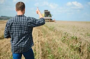 Handsome farmer with tablet standing in front of combine harvester during harvest in field. photo