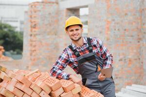 construcción masón trabajador albañil instalando rojo ladrillo con paleta masilla cuchillo al aire libre. foto