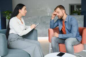 Psychologist talking with patient on therapy session. Depressed man speaking to a therapist while she is taking notes. photo