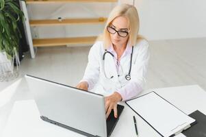Portrait shot of middle aged female doctor sitting at desk and working in doctor office photo