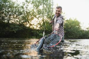 Man with fishing rod, fisherman men in river water outdoor. Catching trout fish in net. Summer fishing hobby photo