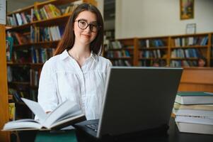 Universidad biblioteca hermosa inteligente caucásico niña usos computadora portátil, escribe notas para papel, ensayo, estudiar para clase asignación. enfocado estudiantes aprendiendo, estudiando para Universidad exámenes lado ver retrato foto