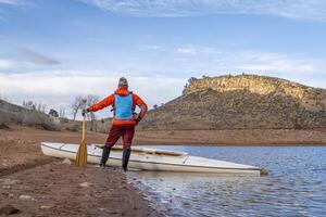 male paddler with a decked expedition canoe and a wooden paddle on a shore of Horsetooth Reservoir in northern Colorado in cold season scenery photo