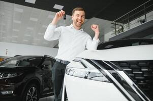 Yes, that's my new car. Customer in car dealership. Young man with keys in hand. photo