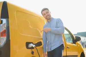 Hansome bearded guy near his new modern electric car at the charging station photo