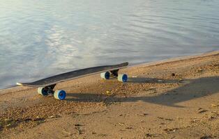 cruising longboard with blue wheels on a lake shore photo