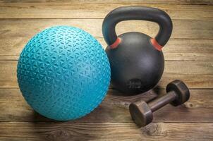 heavy rubber slam ball filled with sand, iron kettlebell and a small dumbbell on a rustic wood background, training, exercise and fitness concept photo