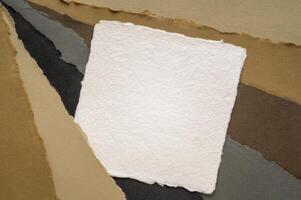 small square sheet of blank white Khadi paper against paper abstract in earth colors photo