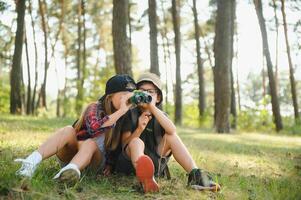 dos contento niños teniendo divertido durante bosque caminata en hermosa día en pino bosque. linda chico explorar con prismáticos durante excursionismo en verano bosque. conceptos de aventura, exploración y excursionismo turismo foto