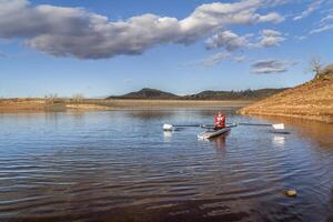 Senior male rower is rowing a coastal rowing shell - Horsetooth Reservoir in fall or winter scenery in northern Colorado. photo