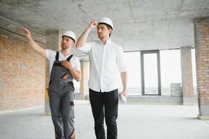 ingeniero y trabajador comprobación proyecto a edificio sitio fondo, construcción sitio a puesta de sol en noche hora foto