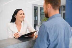 The employee of the beauty salon meets the client in the reception of a modern beauty salon. A man signs a paper with the consent for maintenance. The woman smiles at him photo