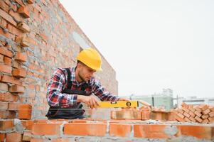 construcción masón trabajador albañil instalando rojo ladrillo con paleta masilla cuchillo al aire libre. foto