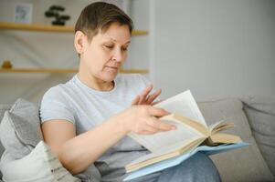 woman in home sitting on sofa reading book. photo