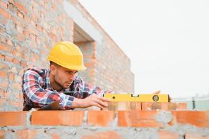 Using bricks. Young construction worker in uniform is busy at the unfinished building photo