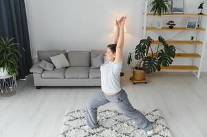 adulto mujer haciendo aptitud ejercicios a hogar. mayor mujer hacer extensión ejercicios. maduro mujer haciendo yoga poses foto