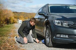 Man with broken down car flat tire in the middle of the street photo