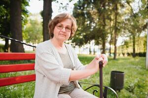 Elegant elderly woman in the shirt is sitting on the bench in a park on a warm day photo