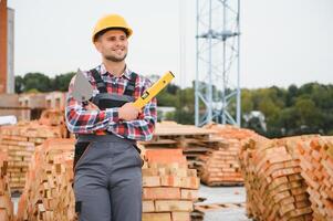 Using bricks. Young construction worker in uniform is busy at the unfinished building photo
