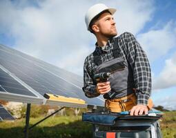 Portrait of smiling confident engineer technician with electrical screwdriver, standing in front of unfinished high exterior solar panel photo voltaic system