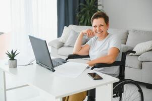 Freelancer in wheelchair using laptop near notebook and papers on table photo